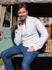 Man sitting on a Land Rover wearing a light gray quarter zip jumper and blue jeans.