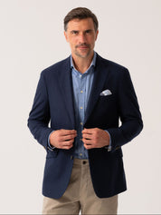 Man wearing a navy wool and cashmere blazer over a light blue shirt with beige trousers on a plain background