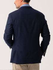 Back view of Man wearing a navy wool and cashmere blazer over a light blue shirt with beige trousers on a plain background