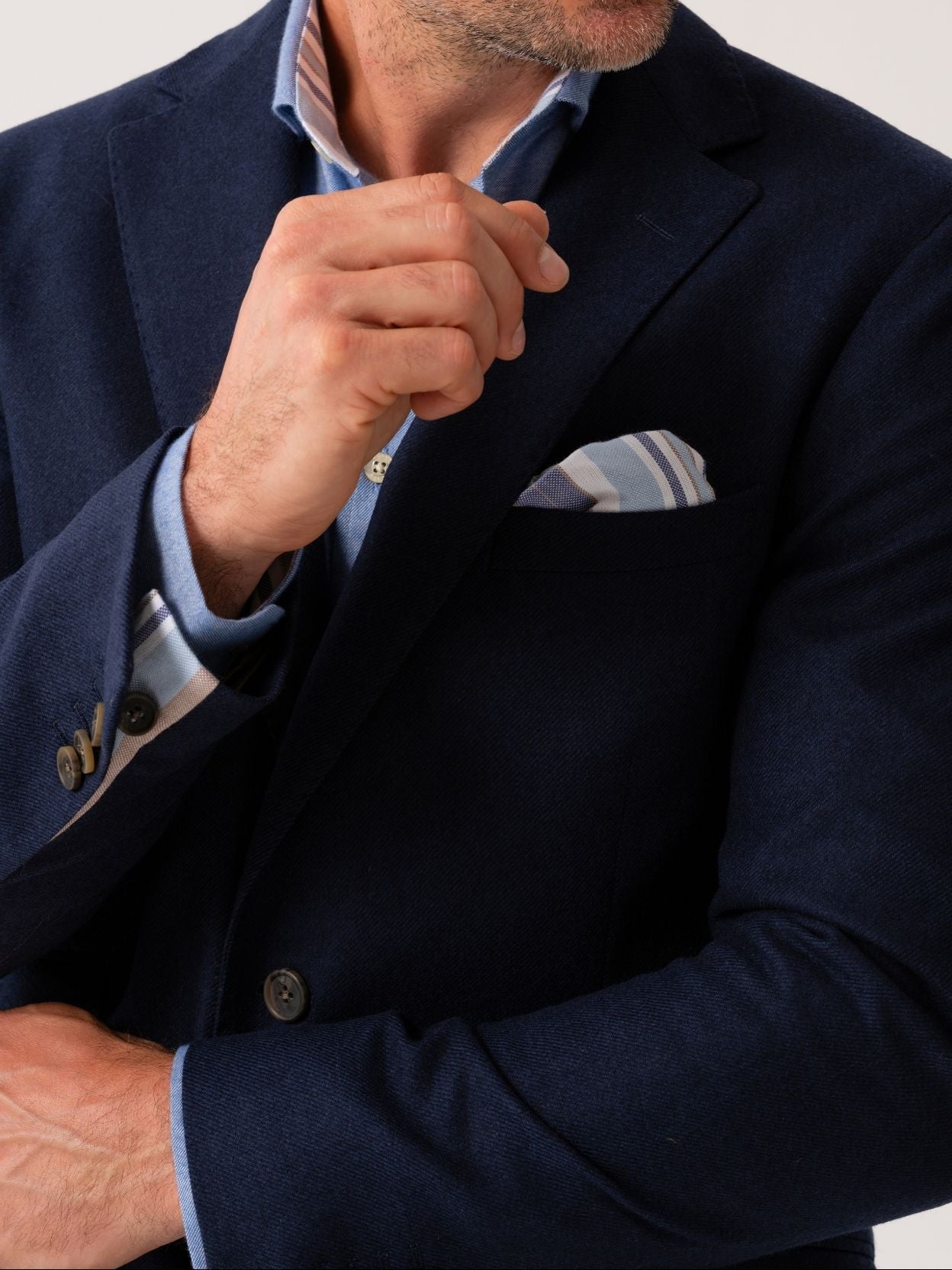 Man wearing a navy wool and cashmere blazer with striped African fabric pocket square on a plain background