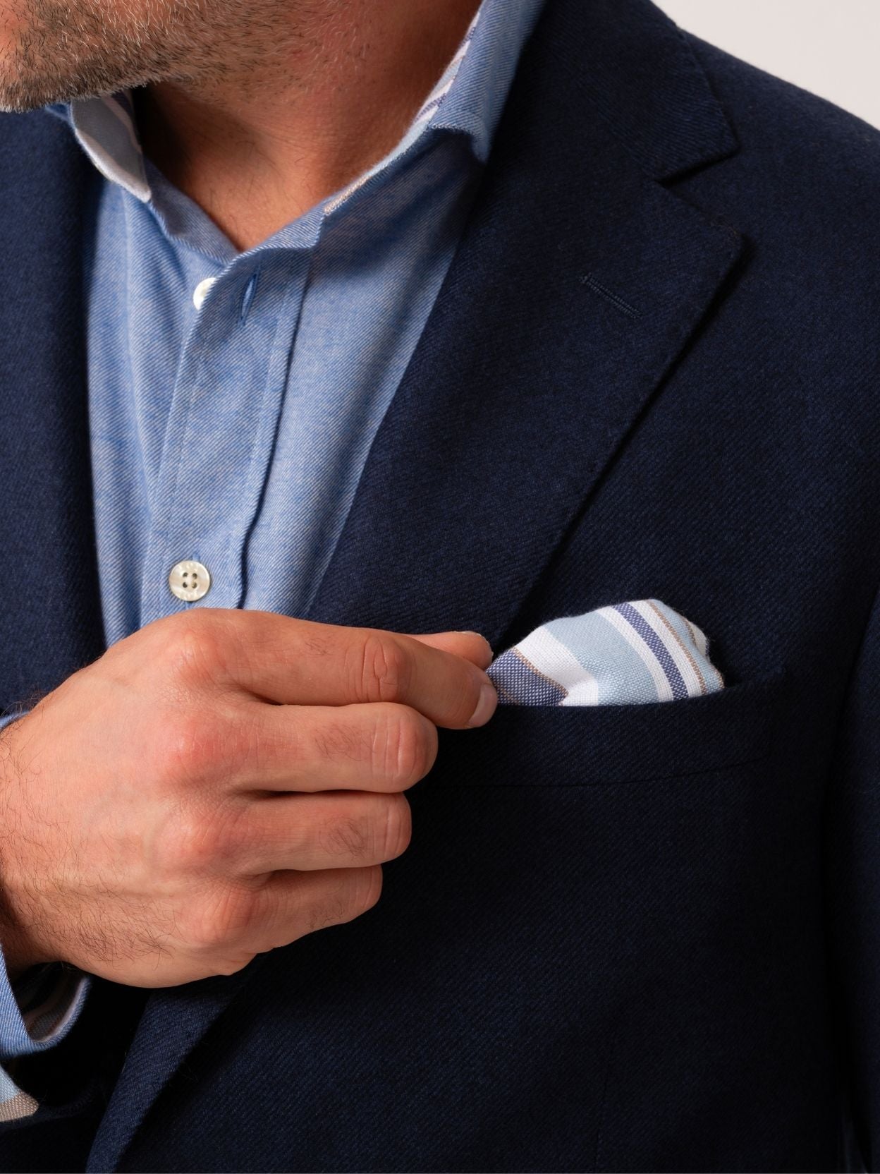 Man wearing a navy wool and cashmere blazer with striped African fabric pocket square on a plain background