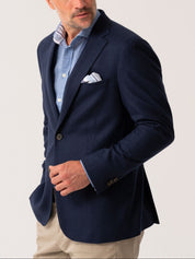 Man wearing a navy blazer over a light blue shirt with a striped pocket square on a plain background