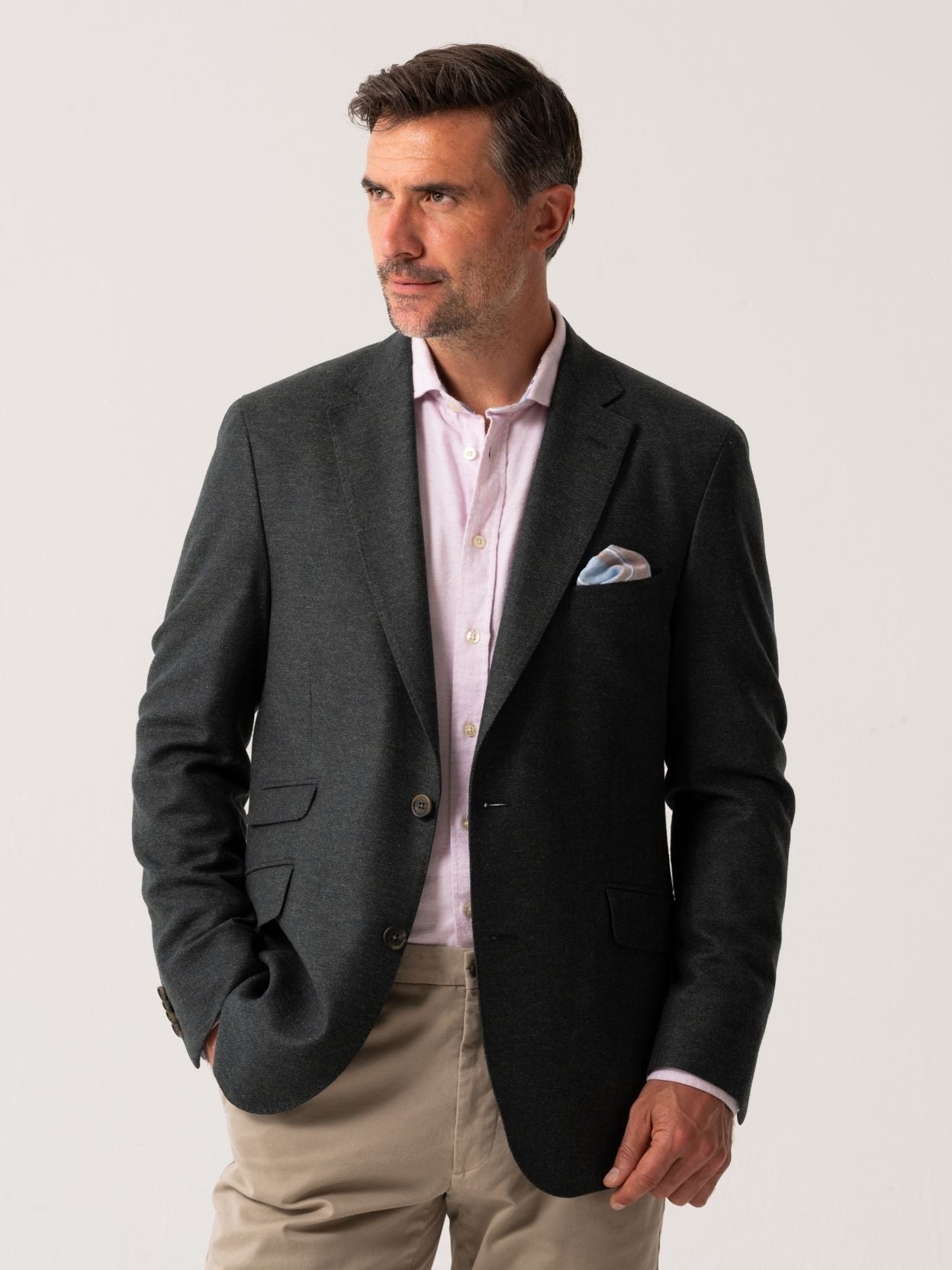 Man wearing an olive blazer over a light pink shirt with beige trousers on a white background