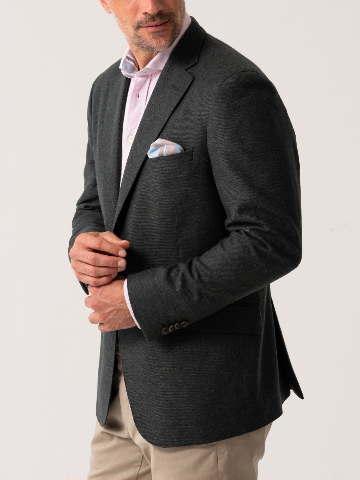 Man wearing an olive blazer over a light pink shirt with beige trousers on a white background