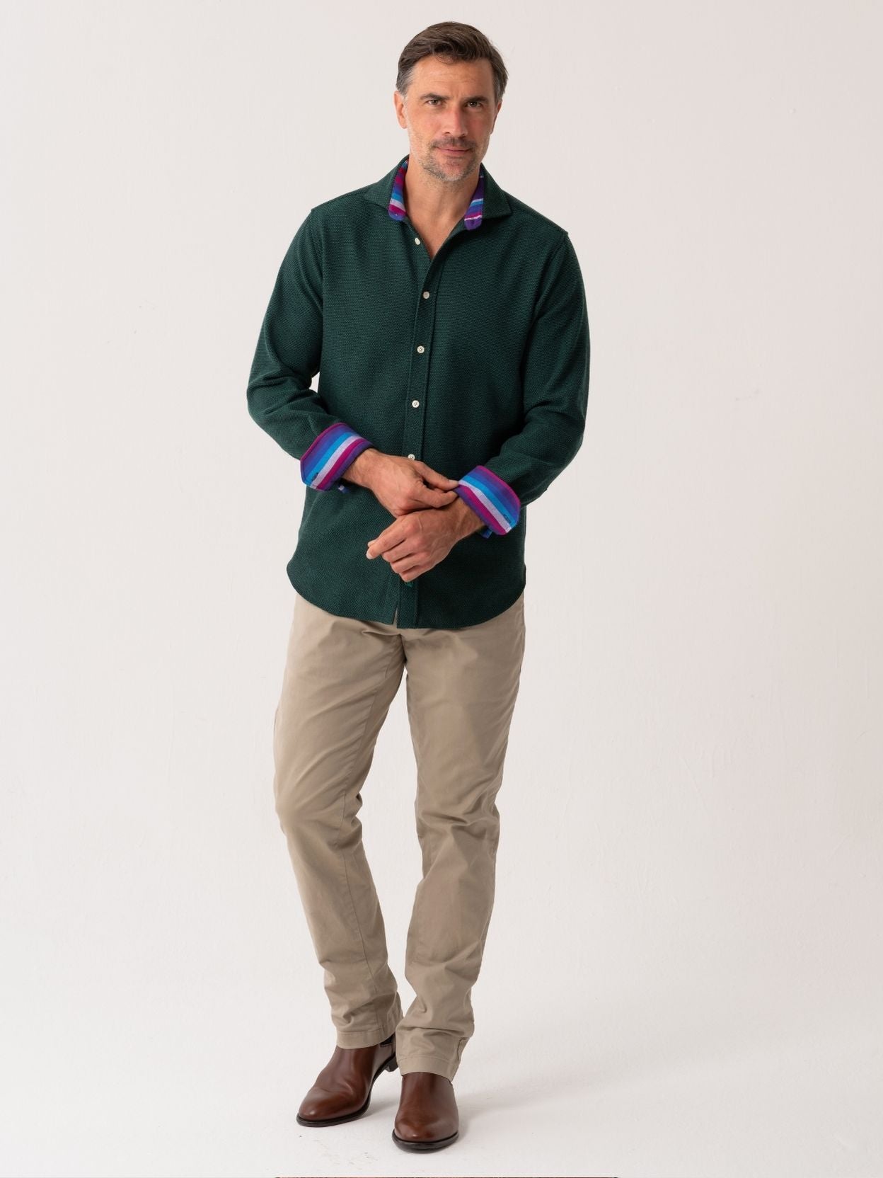 Man wearing a dark green shirt with colorful cuffs and beige trousers on a white background