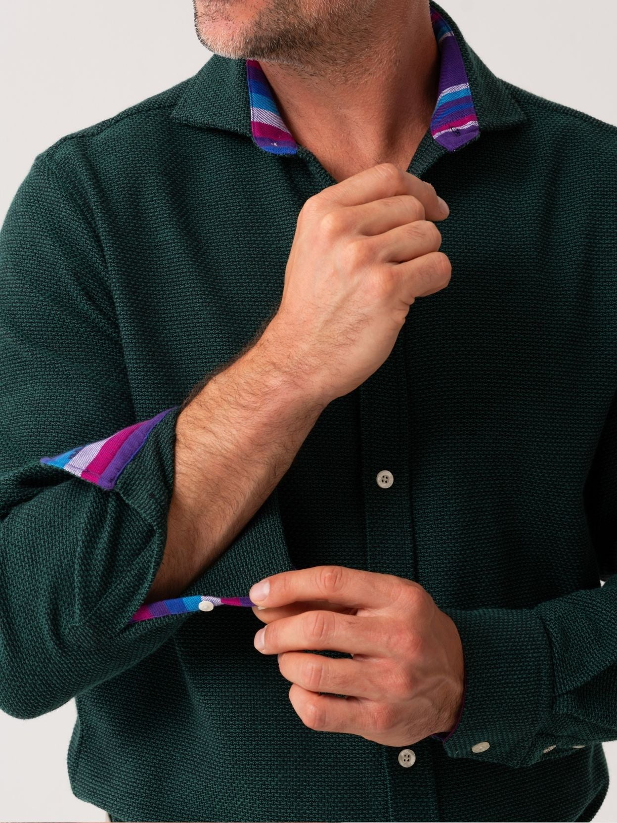Man adjusting the collar of a dark green shirt with colourful cuffs.