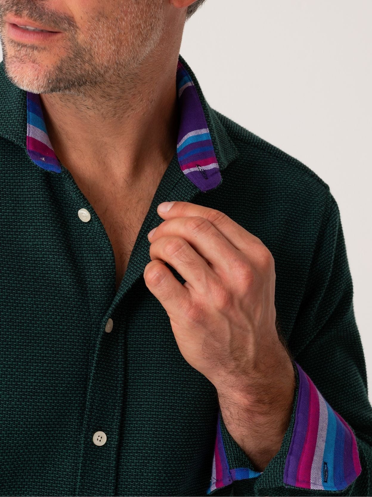 Man wearing a dark green shirt with colorful collar and cuffs against a neutral background