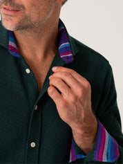 Man wearing a dark green shirt with colorful collar and cuffs against a neutral background