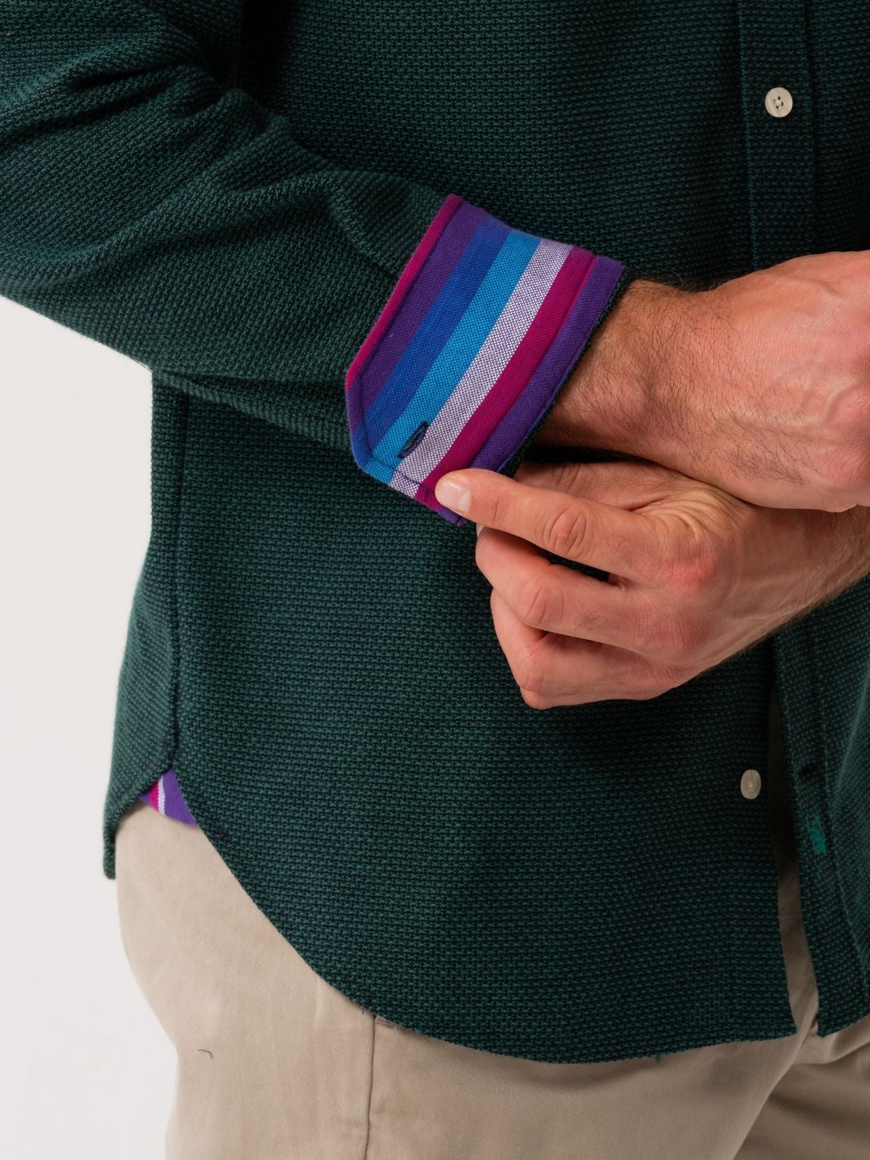 Person wearing a dark green shirt with a colorful striped sleeve cuff.
