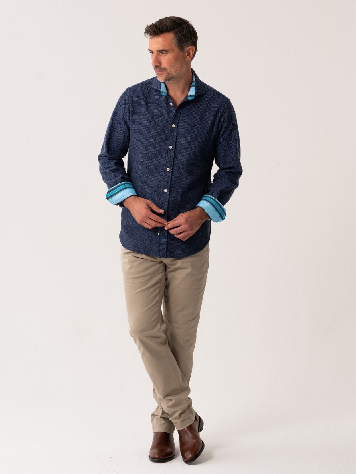 Man wearing a navy shirt with blue trim and beige pants on a white background