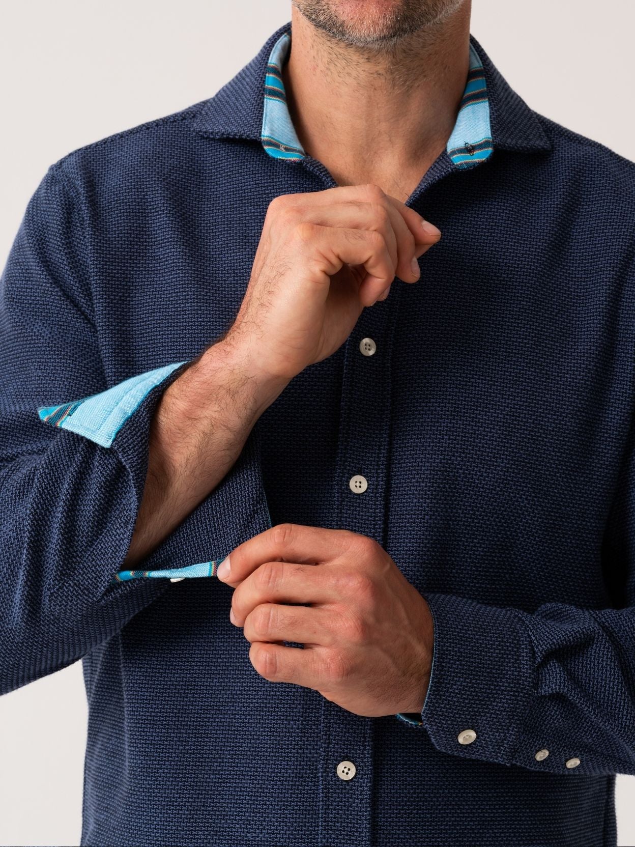 Person wearing a navy blue textured shirt with light blue collar and cuffs on a white background