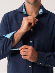Person wearing a navy blue textured shirt with light blue collar and cuffs on a white background