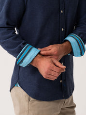 Person wearing a navy shirt with blue cuffs and trim on a light gray background