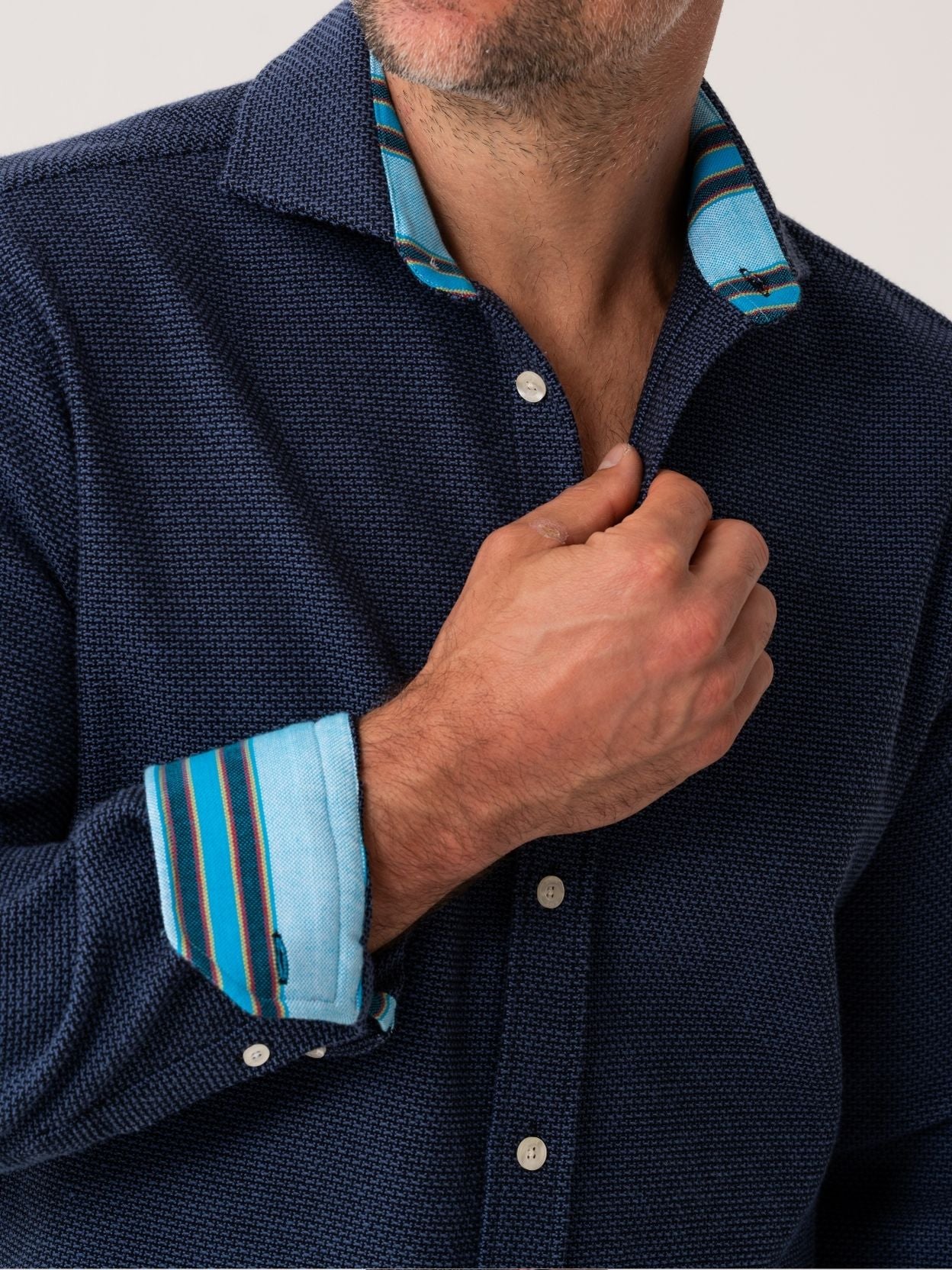 Man wearing a navy shirt with blue striped cuffs and collar.