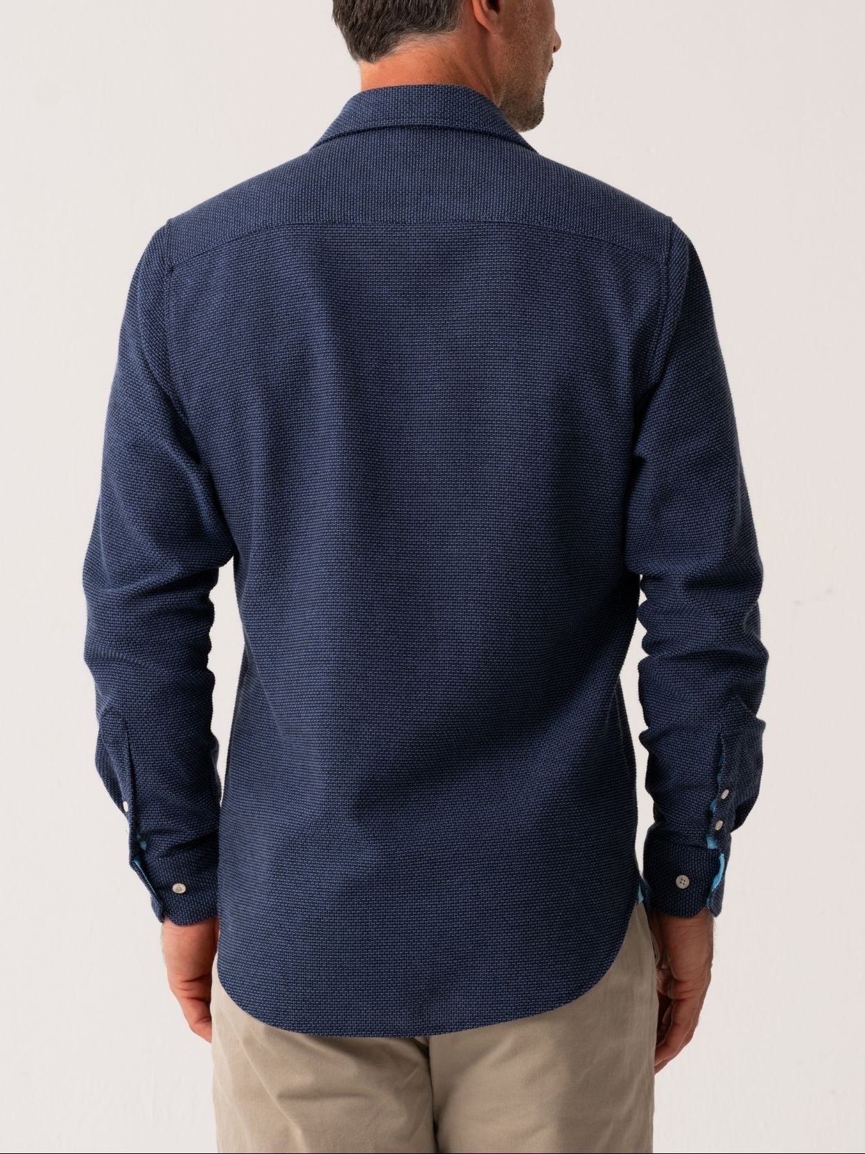 Man wearing a blue shirt from behind on a plain background