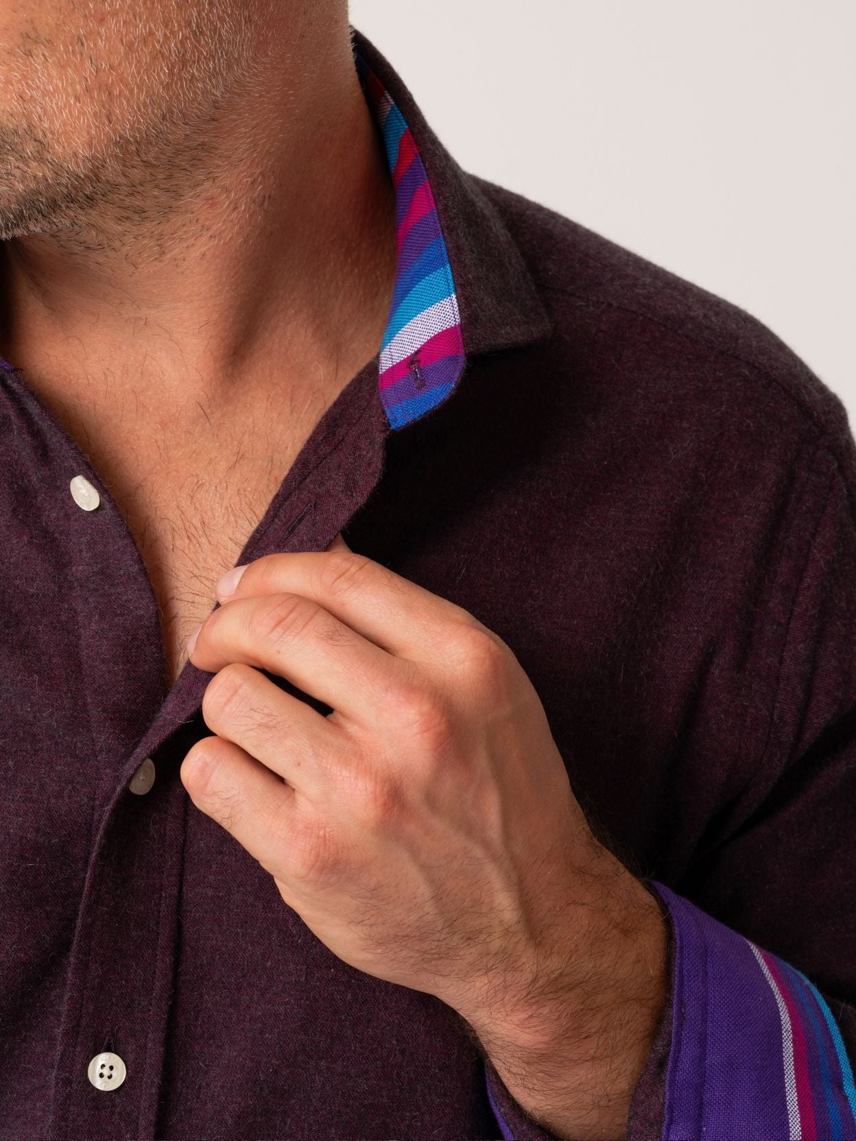Close-up of a person buttoning a dark Burgundy Cotton-Cashmere shirt with a colourful collar.