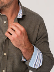 Man wearing an Olive Cotton-Cashmere shirt with a striped cuff, adjusting his collar against a neutral background