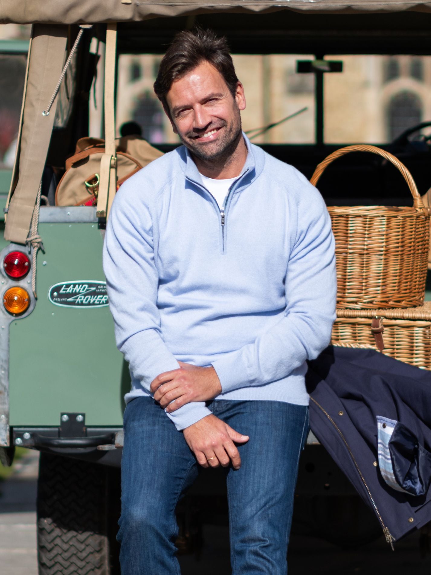 Man sitting in front of a vintage Land Rover wearing a light blue cashmere jumper