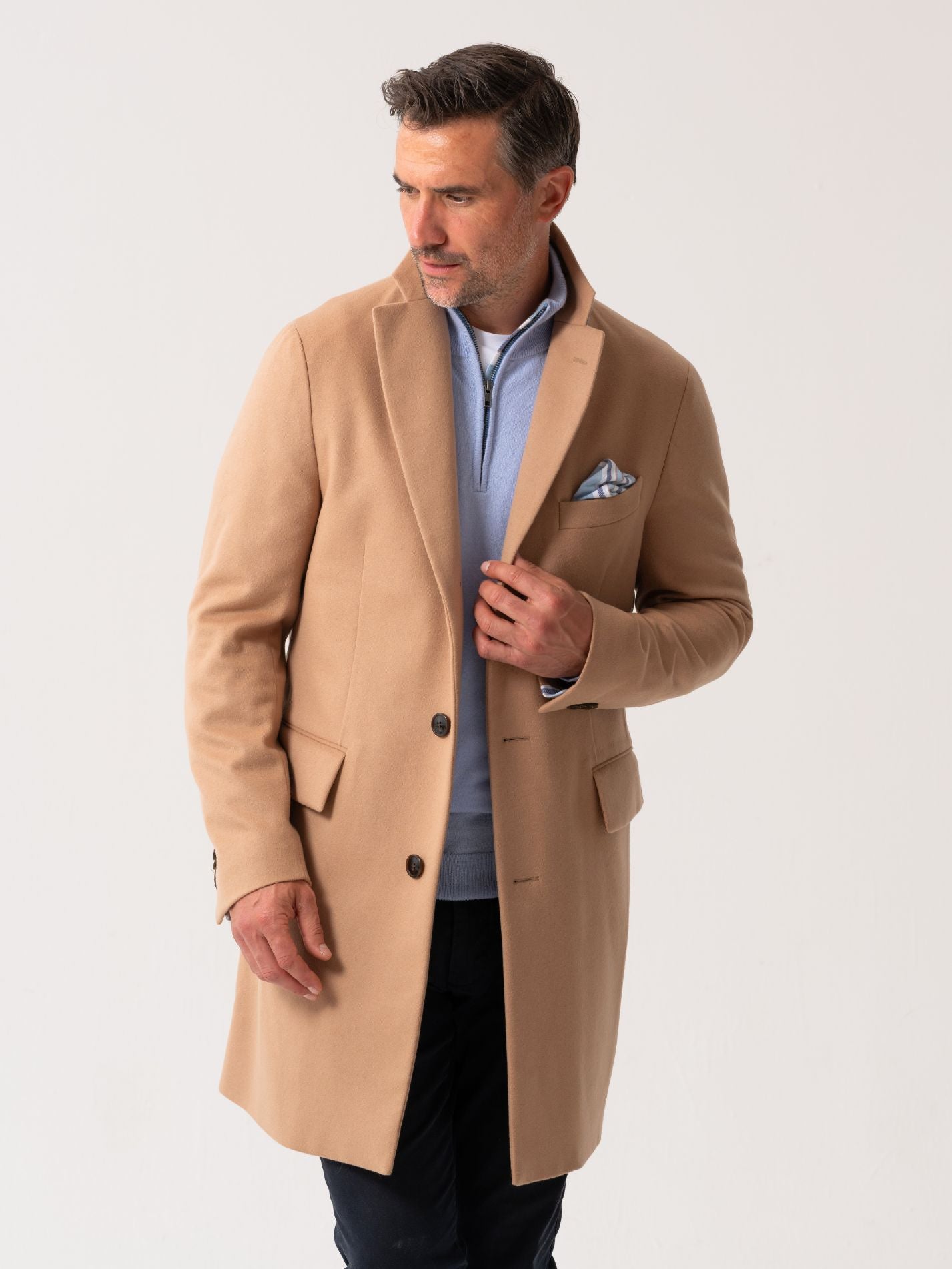 Men’s camel wool overcoat with notch lapel, worn over light blue quarter-zip jumper