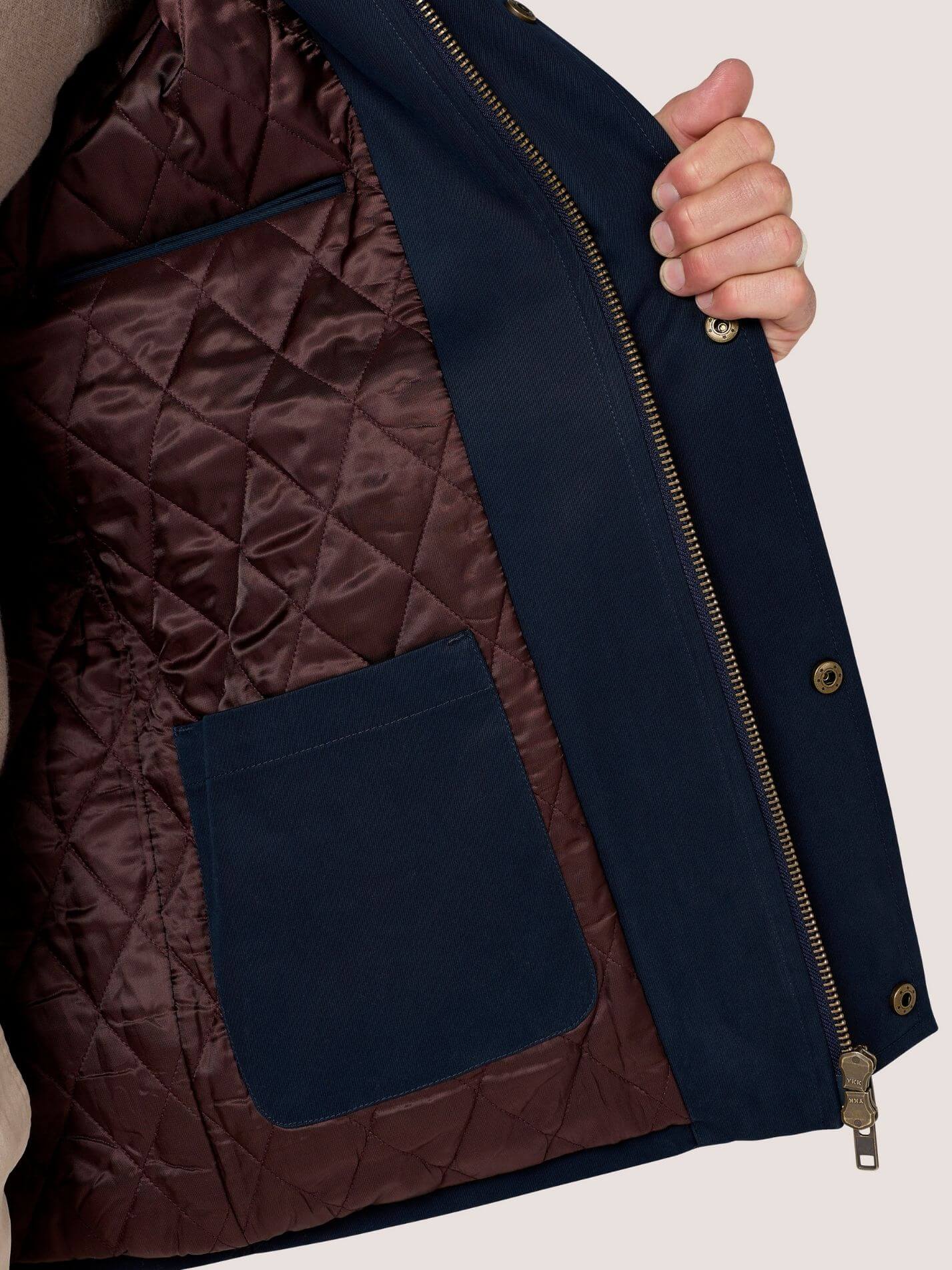 Close-up of a navy blue jacket with a dark brown quilted interior lining and a hand holding the open flap to show the lining.