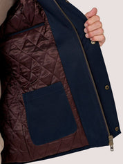 Close-up of a navy blue jacket with a dark brown quilted interior lining and a hand holding the open flap to show the lining.