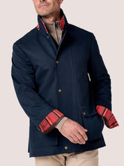 A man wearing a navy blue jacket with a high stand collar and contrasting red, orange, and yellow striped inner lining visible at the collar and cuffs, paired with beige trousers against a light gray studio background.