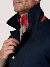 Close-up of a man wearing a navy blue jacket with a high collar, a red and purple plaid inner lining visible at the collar, and a beige knit shirt underneath.