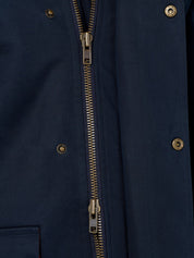 Close-up of a navy blue jacket with a central brass double-zipper and matching brass snap buttons.