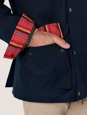 Close-up of a navy blue jacket with a large front patch pocket and a striped red, yellow, and blue cuff, worn by a model with khaki pants.
