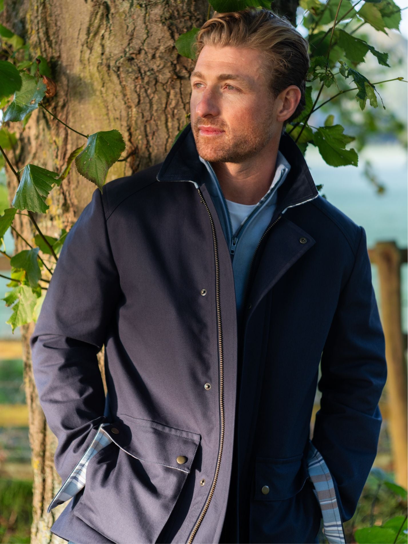 Mens navy outerwear coat with water resistant finish - front view standing outside under a tree