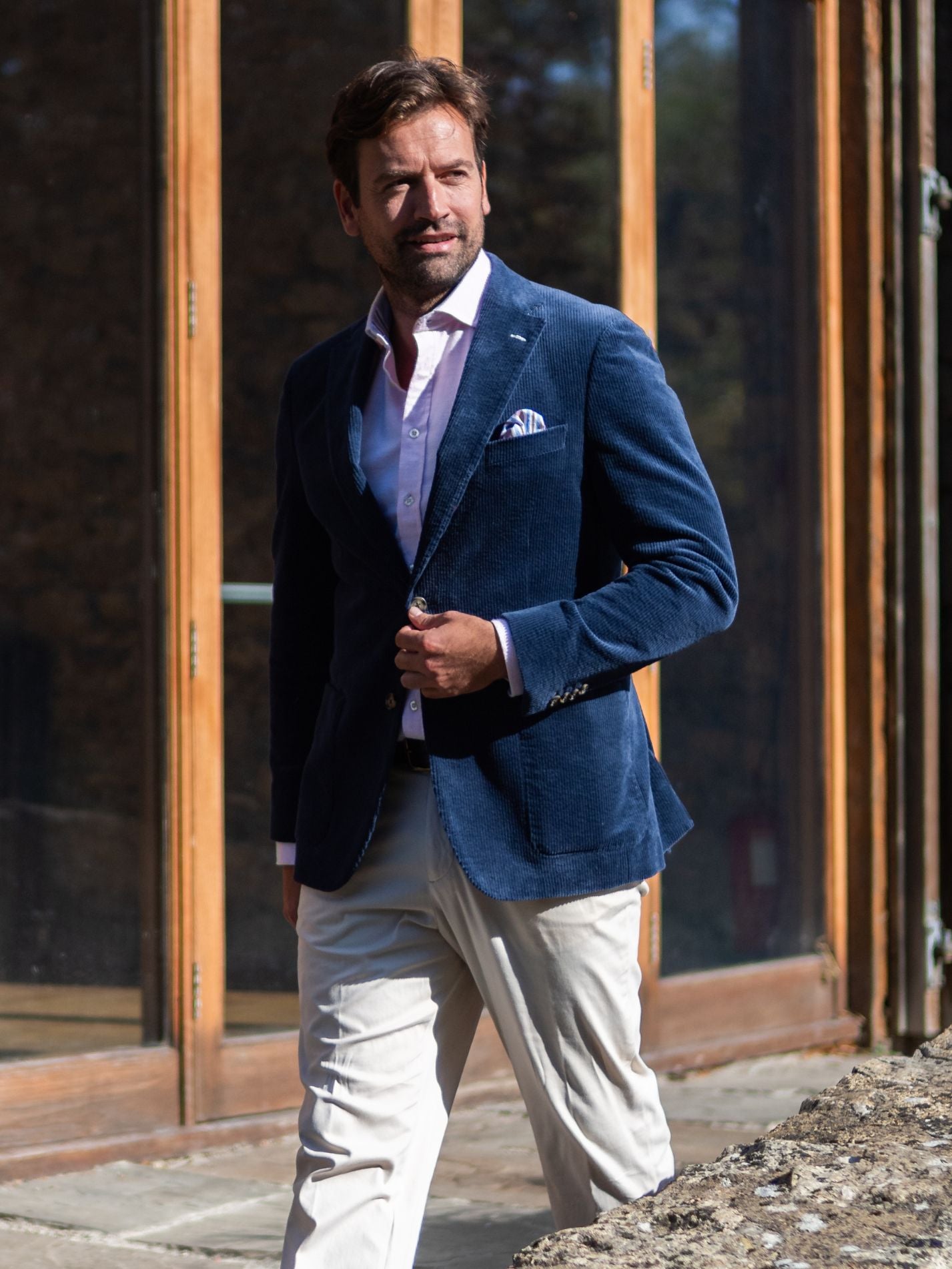Man wearing a navy blue corduroy blazer and light beige chinos standing outdoors.