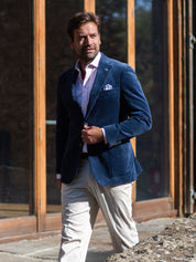 Man wearing a navy blue corduroy blazer and light beige chinos standing outdoors.