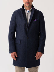 Men’s navy wool herringbone overcoat with notch lapel, worn over light grey quarter-zip jumper