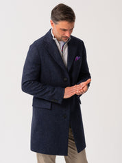 Men’s navy wool herringbone overcoat with notch lapel, worn over light grey quarter-zip jumper