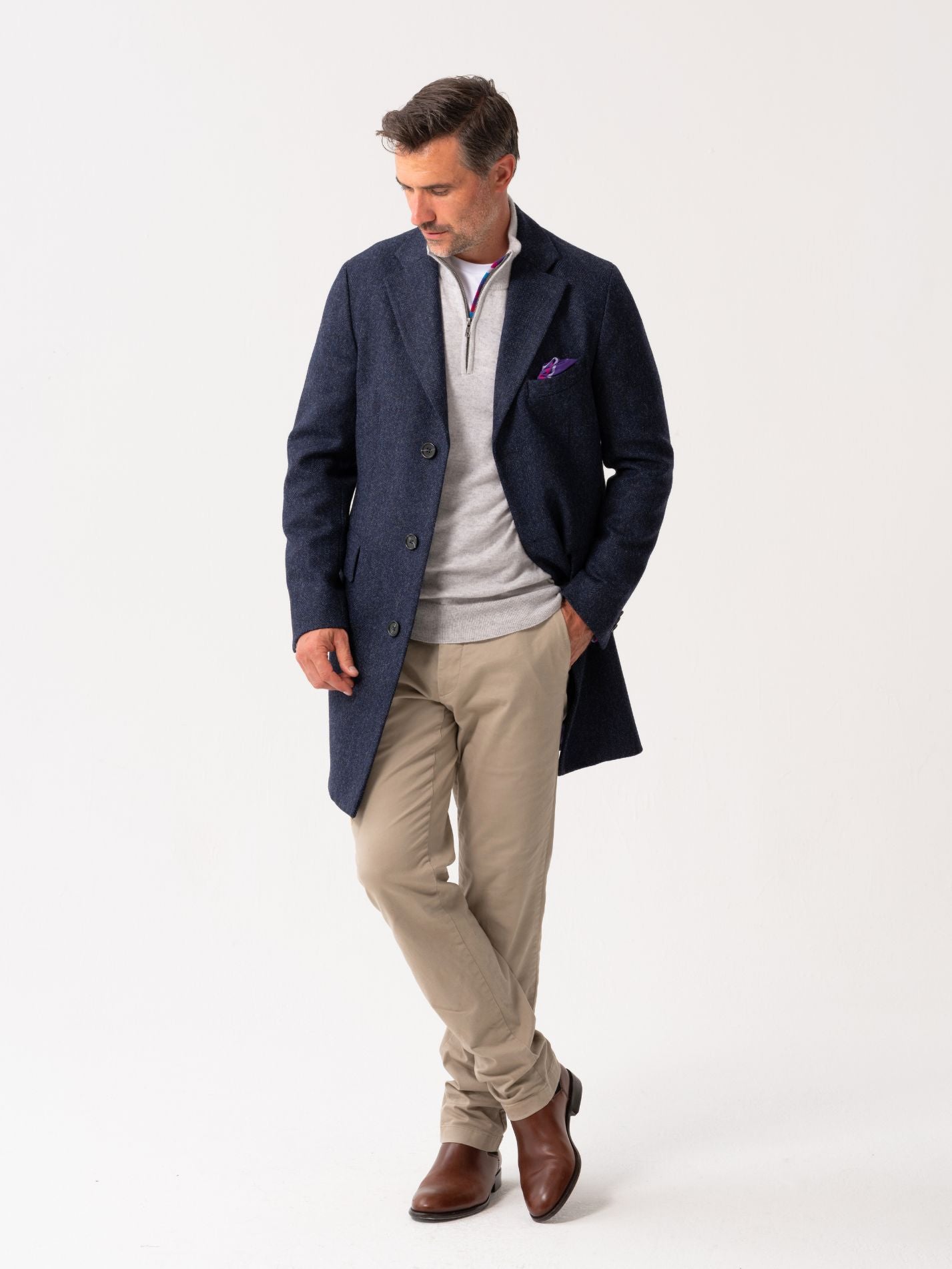 Full body look of Men’s navy wool herringbone overcoat with notch lapel, worn over light grey quarter-zip jumper