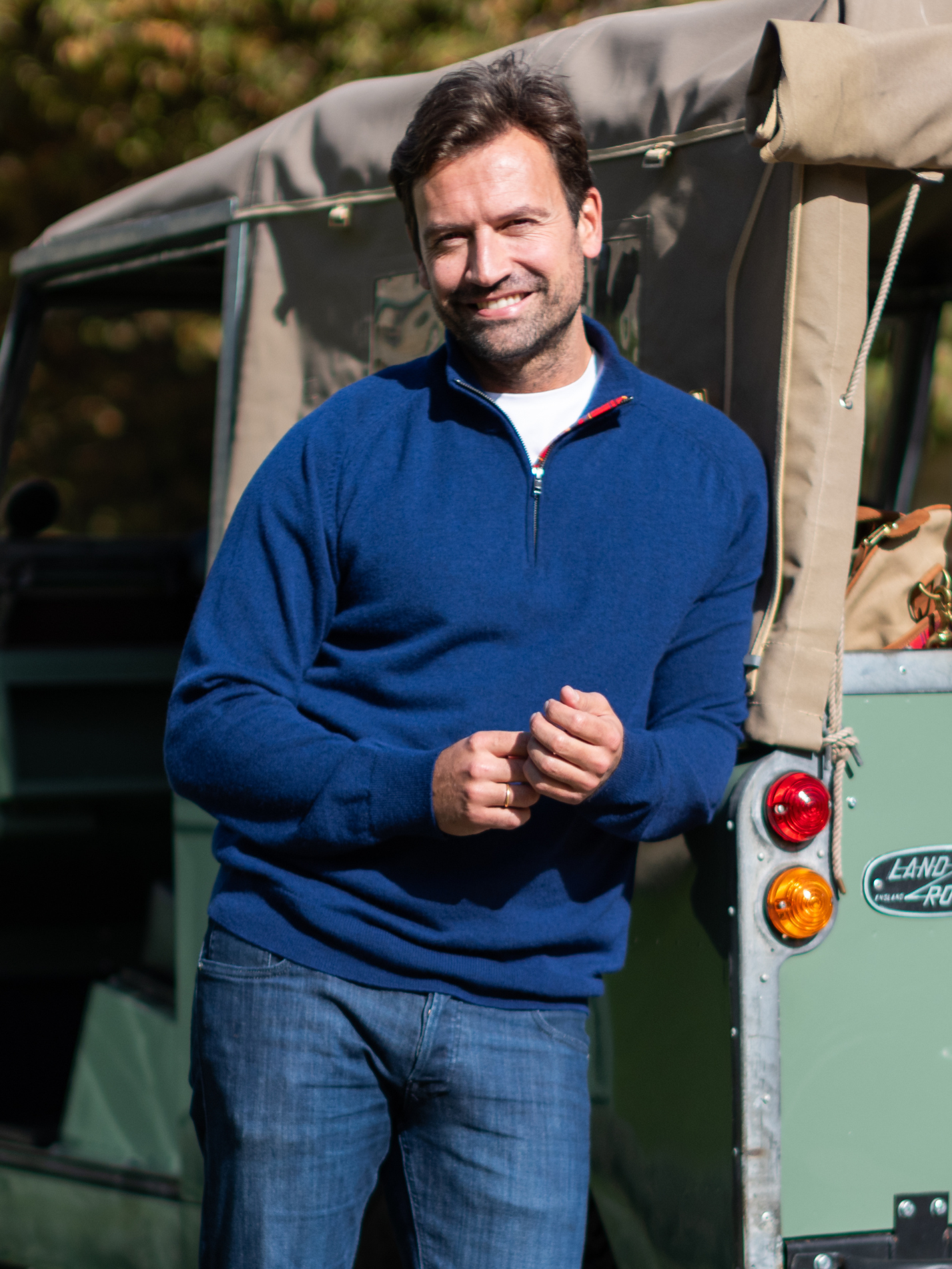 Man in a navy blue quarter zip jumper standing next to a Land Rover vehicle