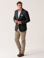 Man wearing an olive blazer over a light pink shirt with beige trousers on a white background