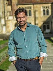 Man in a petrol blue shirt and navy chinos walking outdoors on a stone path.