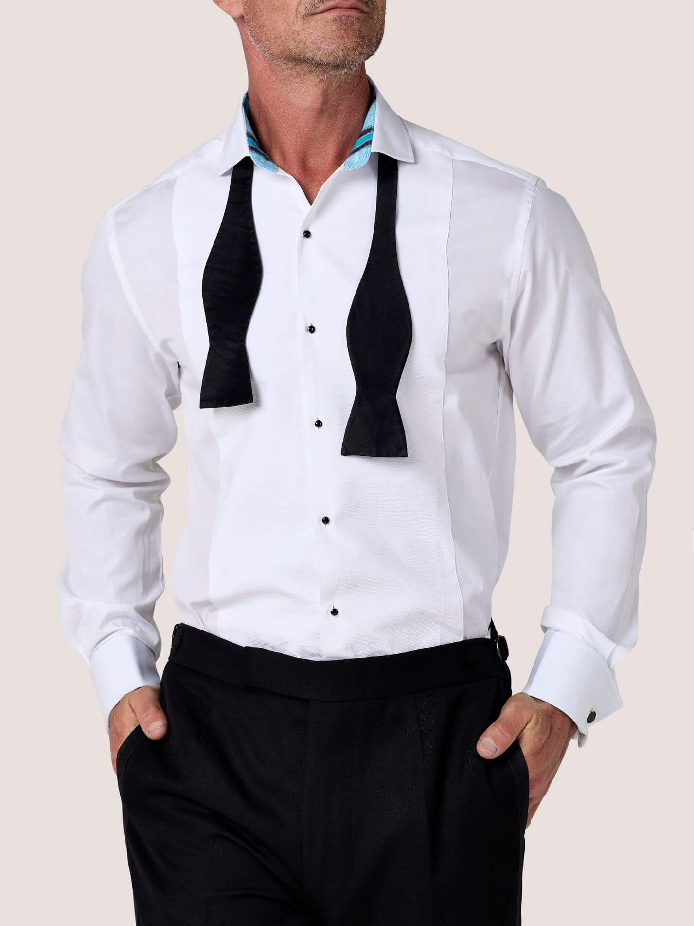 Koy white dress shirt with black bow tie loosely untied, hands in trouser pockets